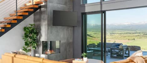 Una sala de estar moderna con un sofá, una chimenea y un ventanal con vistas a un paisaje pintoresco.