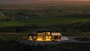 A modern house with a large glass facade, situated in a rural area with expansive fields and a clear sky. - Basecamp Stays: Lux Retreat, Epic Views, & Hot Tub (Tetonia)