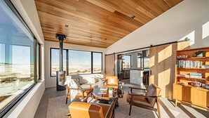 A modern living room with large windows, a wooden ceiling, and a bookshelf. - Basecamp Stays: Lux Retreat, Epic Views, & Hot Tub (Tetonia)