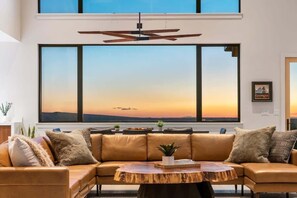 A modern living room with a large window, leather sofa, and a wooden coffee table. - Basecamp Stays: Lux Retreat, Epic Views, & Hot Tub (Tetonia)