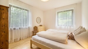 Une chambre avec un lit en bois, des rideaux blancs, une petite commode en bois et un miroir rond.