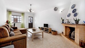 A living room with a sofa, a table, a TV, a fireplace, and decorative plates on the wall. - Holiday Home 'Brita' with Private Terrace, Balcony and Wi-Fi (Raposeira)