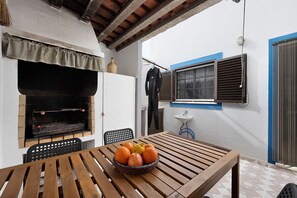 A wooden table with a basket of fruit, a grill, and a chair. - Holiday Home 'Brita' with Private Terrace, Balcony and Wi-Fi (Raposeira)