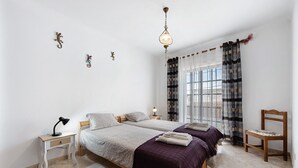 A bedroom with two beds, a nightstand, a chair, a lamp, and a window with curtains. - Holiday Home 'Brita' with Private Terrace, Balcony and Wi-Fi (Raposeira)