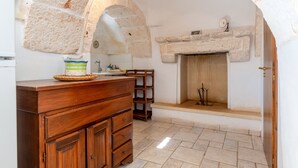 Une cuisine aux murs de pierre, avec un comptoir en bois, une cheminée en pierre et un sol carrelé.