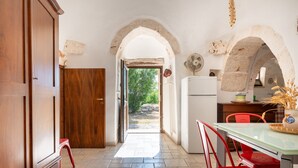 Une cuisine avec une arche ouverte donnant sur un jardin, une table à manger avec des chaises et un réfrigérateur.
