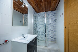 Un baño con cabina de ducha de vidrio, un lavabo blanco y techo de madera.