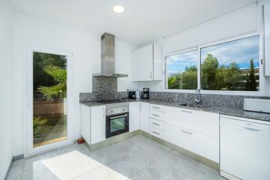 A modern kitchen with white cabinets, a built-in oven, a coffee maker, and a dishwasher.