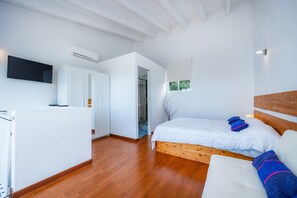 A bedroom with a wooden bed, white walls, a mounted TV, and an air conditioning unit.