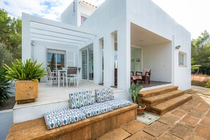 Un patio moderno al aire libre con una zona de estar, una mesa de comedor y una escalera que lleva a un nivel superior.