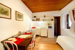 A compact room with a wooden ceiling, a dining table with chairs, a bed, a kitchenette, and a door leading to another room. - Apartment 'Cascina Des Religieuses - Tilleul' with Mountain View, Private Terrace and Wi-Fi (Sarre)