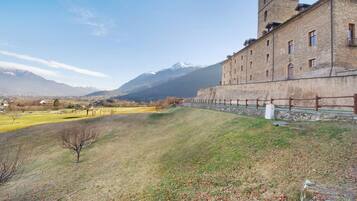 Un edificio histórico con una torre, una colina cubierta de pasto y montañas al fondo.