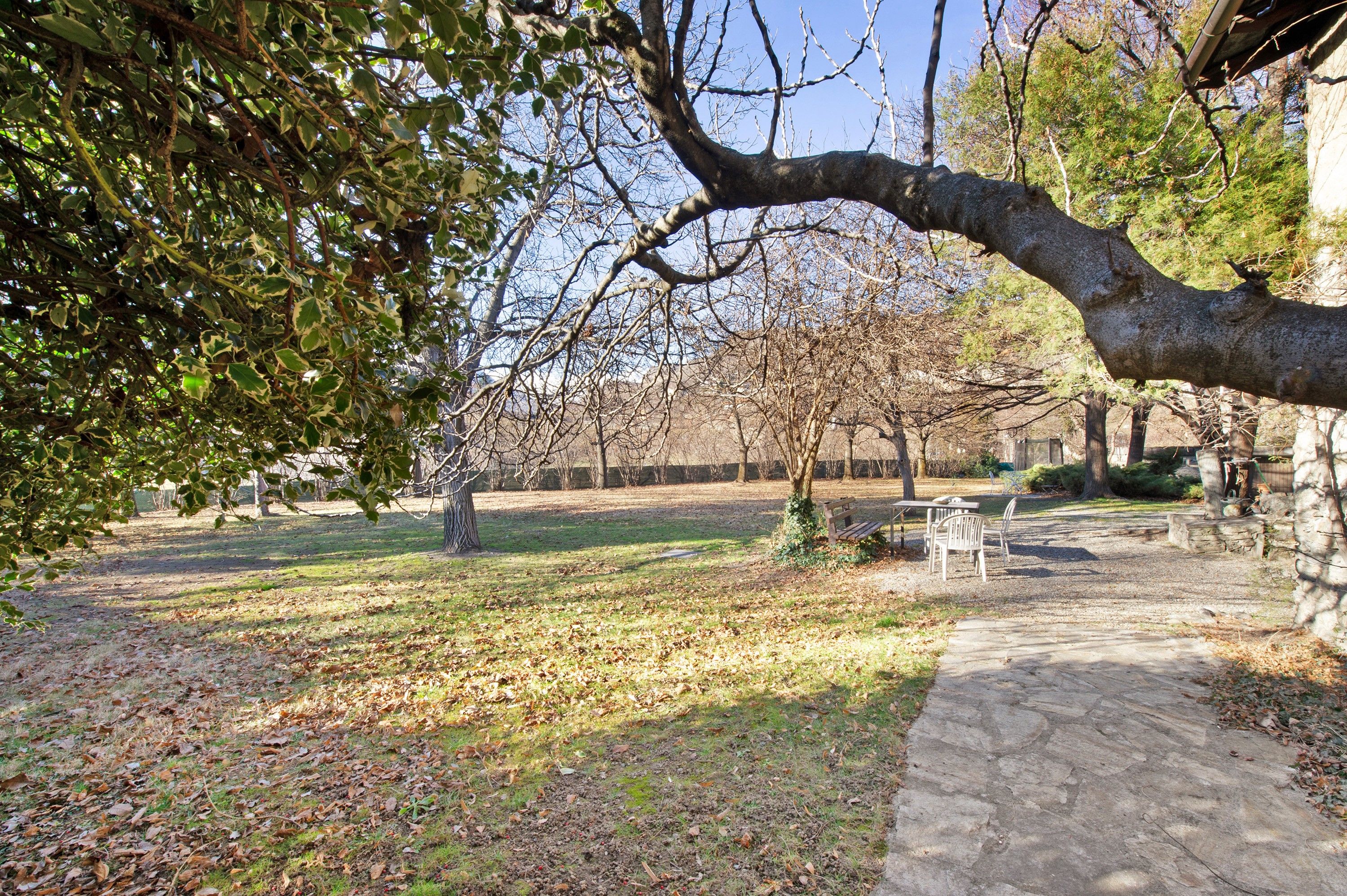 Un parc avec un sentier en pierre, des bancs et un sol recouvert de feuilles.