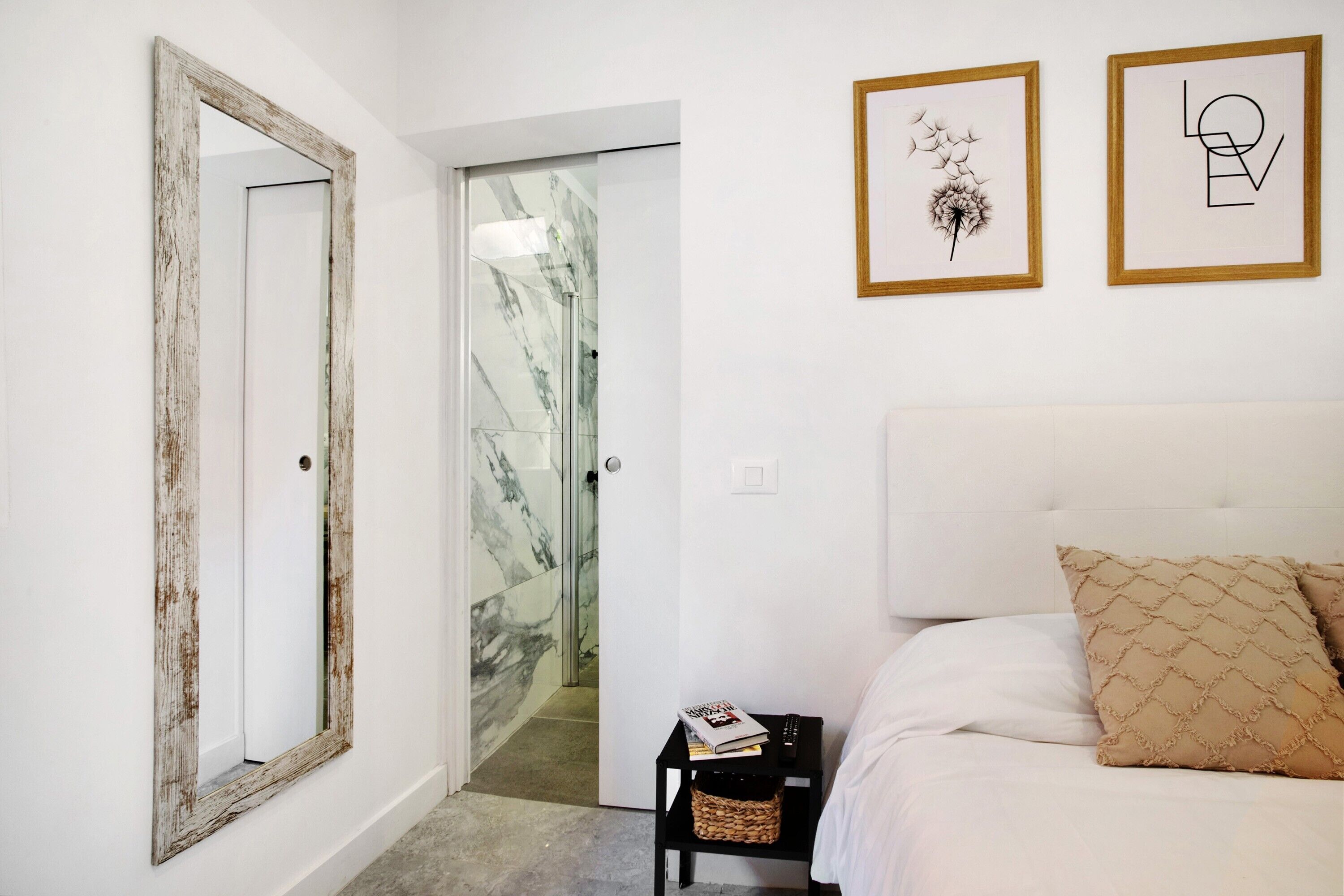 Un dormitorio con una cama, una mesita de noche, un espejo y dos cuadros en la pared.