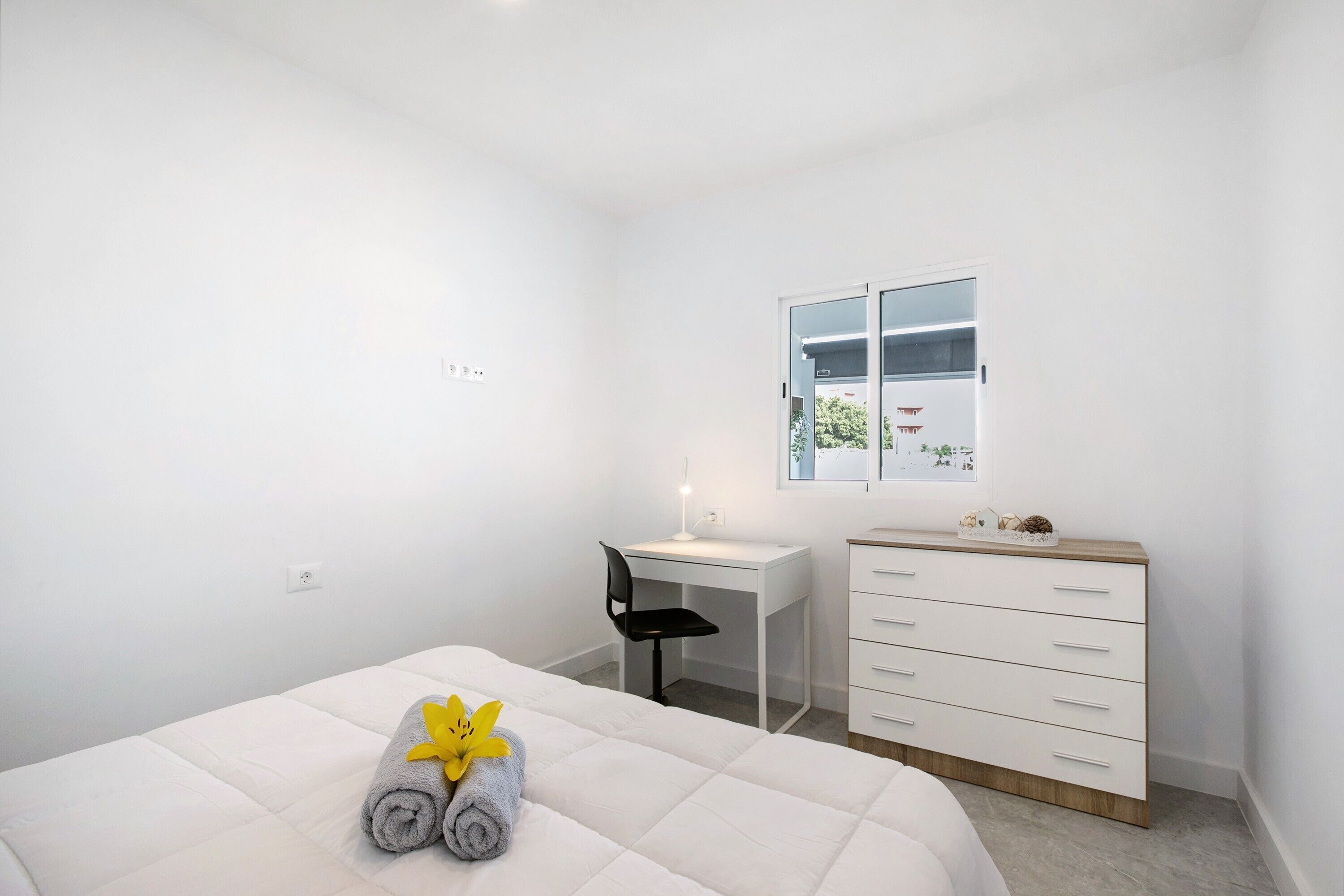 A hotel room with a bed, a desk, a chair, a dresser, and a window with a view.