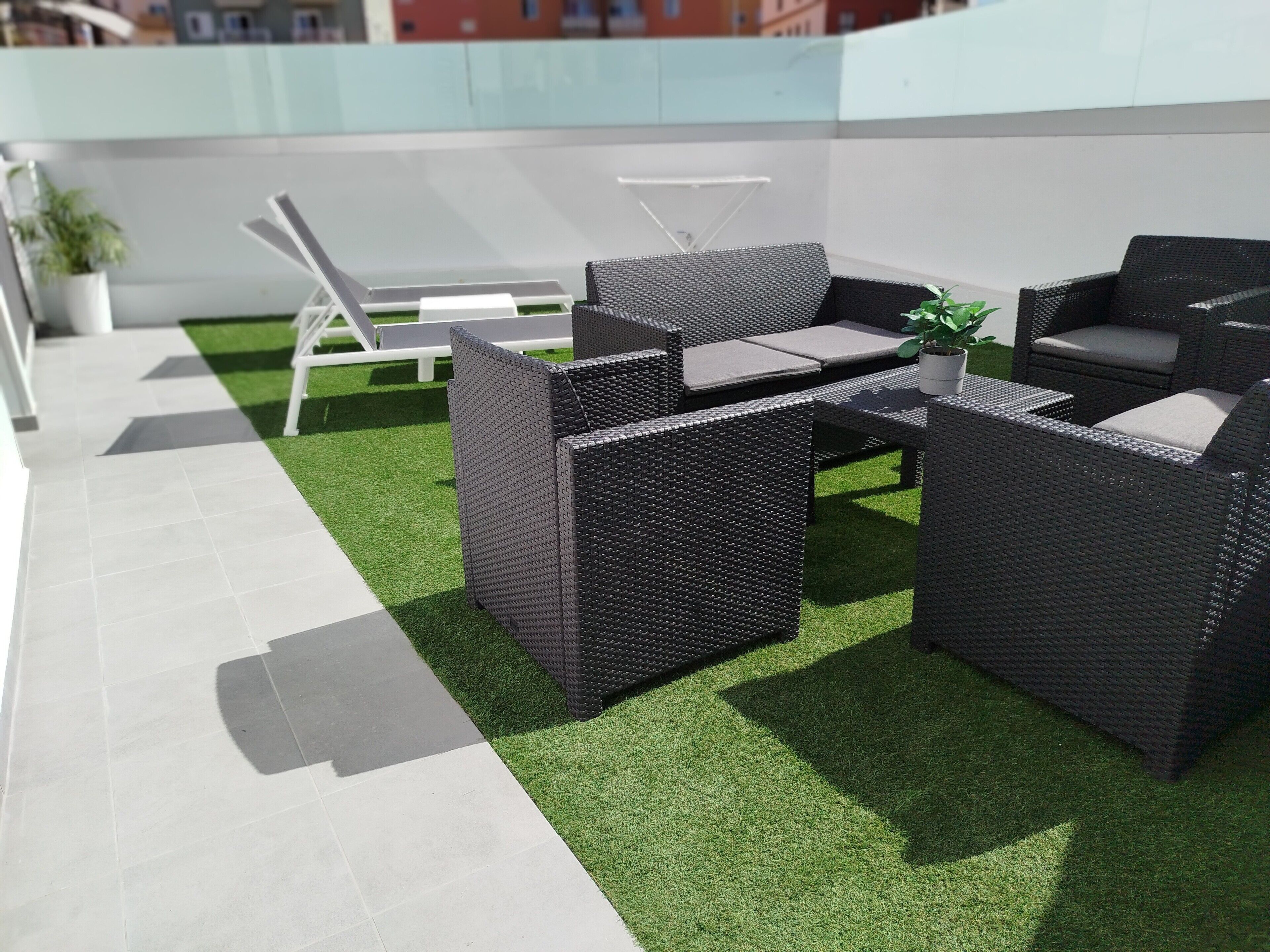 Una terrazza sul tetto con mobili in vimini, prato sintetico e una poltrona da relax bianca.