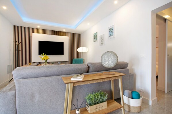 A modern living room with a sectional sofa, a flat-screen TV, a wooden coffee table, a floor lamp, and a decorative wall piece.
