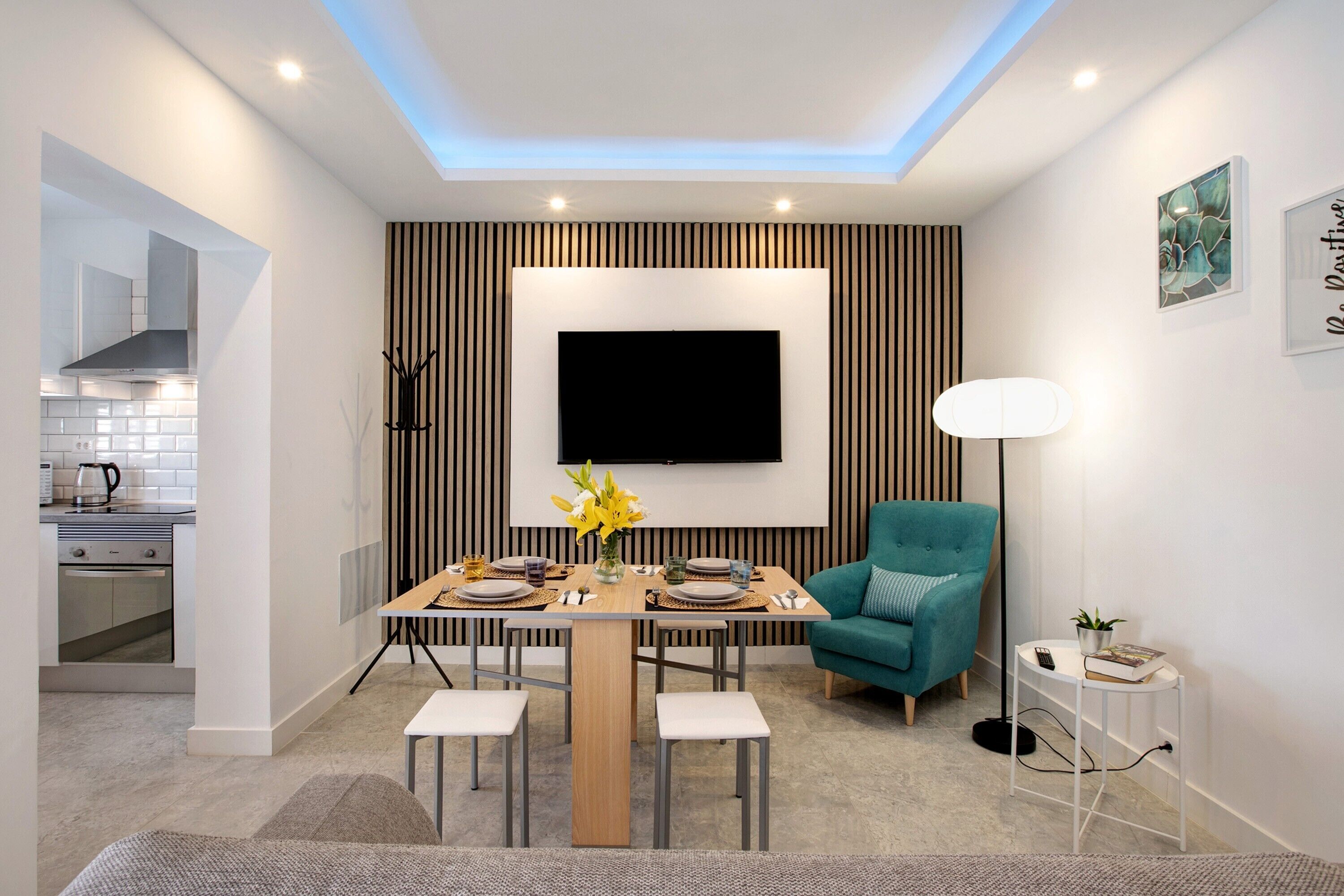 Un comedor moderno con una mesa de madera, sillas, un televisor en la pared y un sillón azul turquesa.