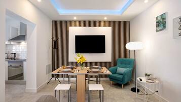 Un comedor moderno con una mesa de madera, sillas, un televisor en la pared y un sillón azul turquesa.