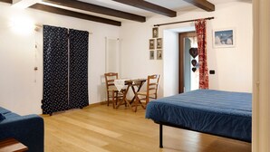 A room with a bed, a table with chairs, a radiator, and a door with curtains.