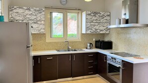 A modern kitchen with dark cabinets, a stainless steel refrigerator, a microwave, and an oven. There are two pendant lights above the sink and a window with a view of greenery outside. - Idyllic Sunsets Seaviews Pool - Villa Melina (Lefkada)
