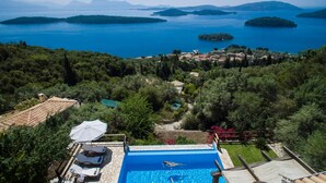 A pool with a view of a lake and islands, surrounded by trees and a small village. - Stunning Seaviews Pool Beach - Pasithea (Lefkada)