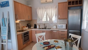 A kitchen with wooden cabinets, a stainless steel refrigerator, a microwave, and a dining table set with food and drinks. - Stunning Seaviews Pool Beach - Pasithea (Lefkada)