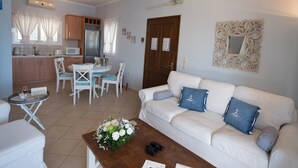A living room with a white sofa, a coffee table with flowers, and a dining area with a table and chairs. - Stunning Seaviews Pool Beach - Pasithea (Lefkada)