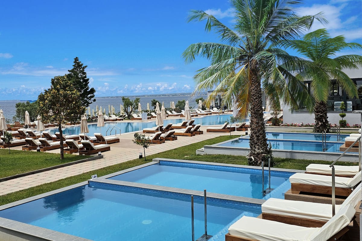 A pool area with multiple sun loungers and palm trees, surrounded by a clear blue sky.