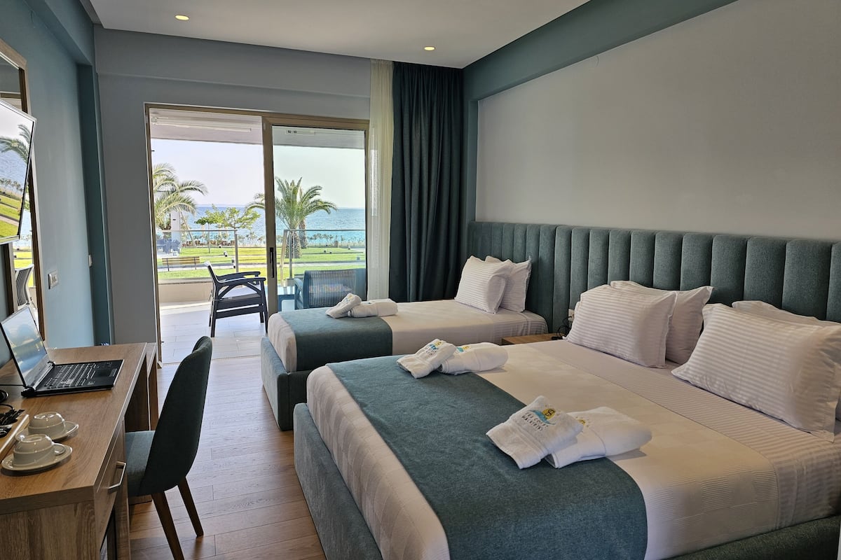 A hotel room with two beds, a desk with a laptop, and a view of the ocean.