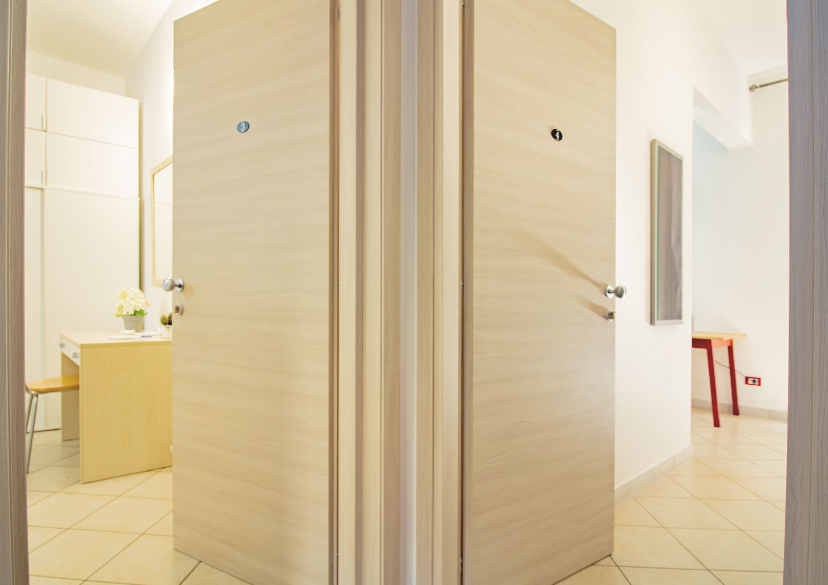 Quarto de hotel com guarda-roupa de madeira, escrivaninha com cadeira, mesa pequena e espelho na parede.