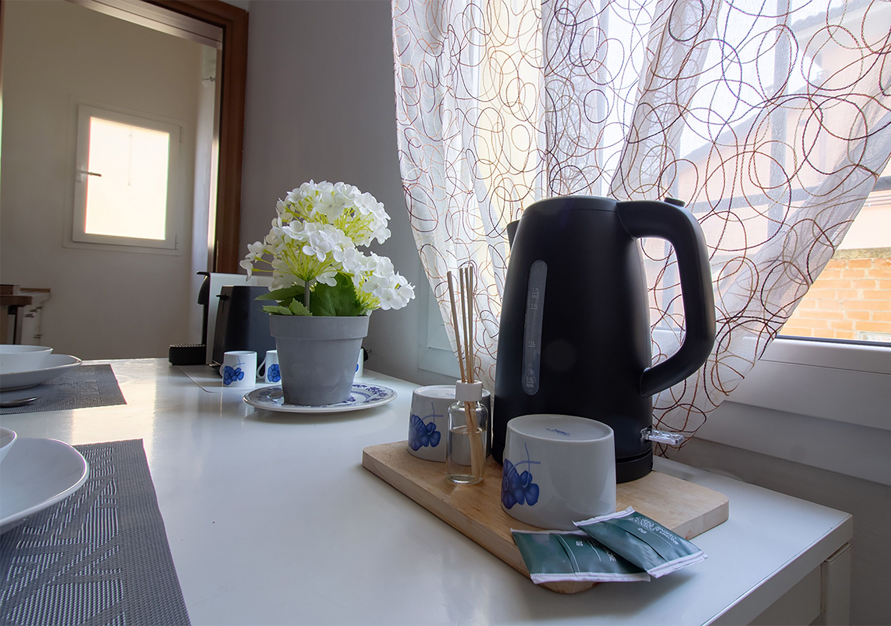Una encimera de cocina con una cafetera, una planta en maceta y una ventana con cortinas estampadas.