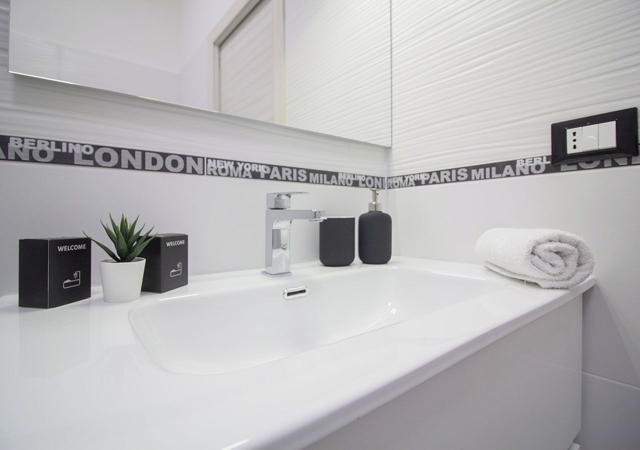 A modern bathroom with a white sink, two black welcome boxes, a potted plant, and a towel.