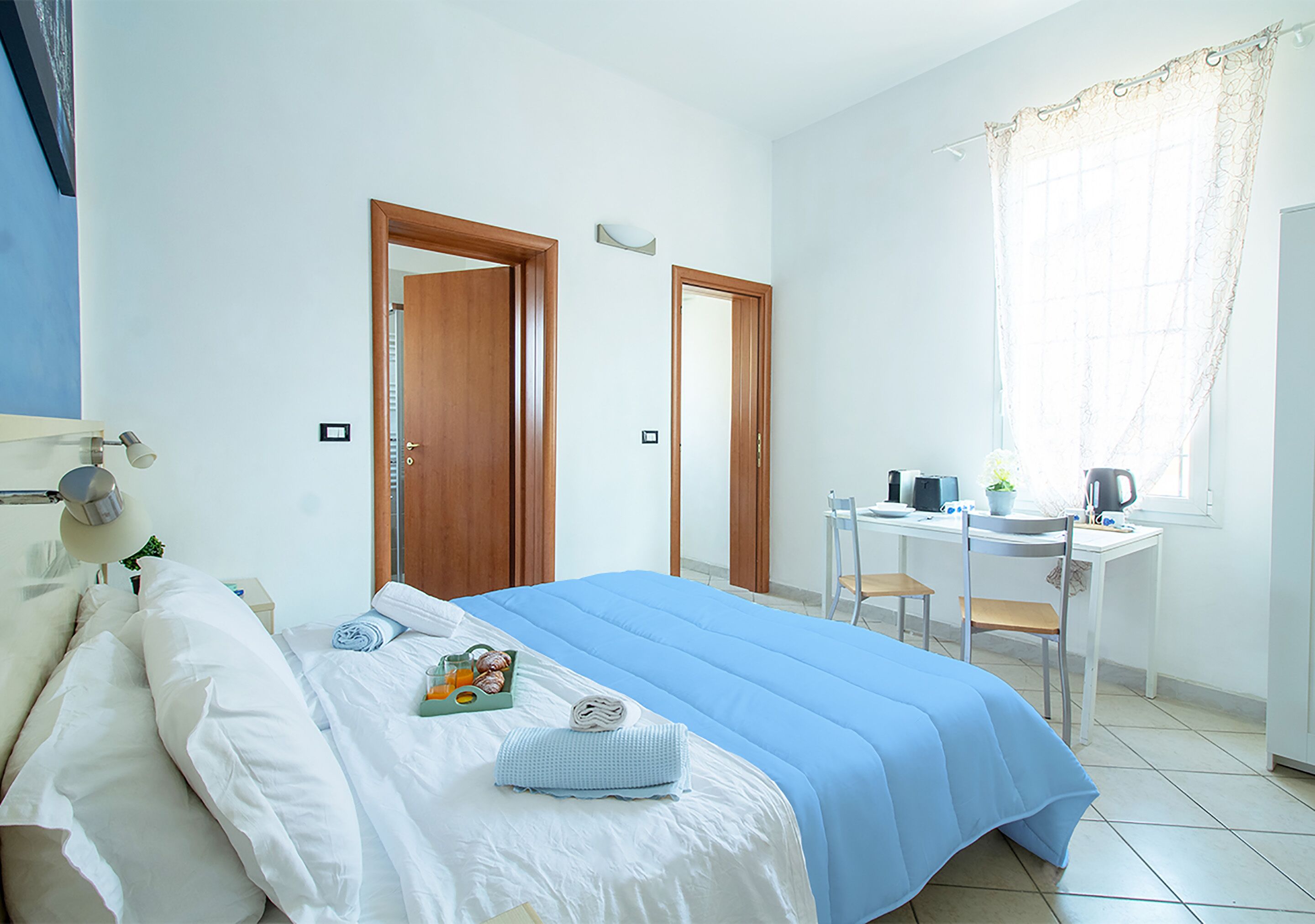 A bedroom with a bed, a desk, and a chair. There is a window with curtains.