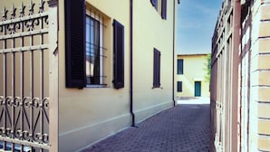 A narrow cobblestone street flanked by buildings with barred windows and a metal gate. - Athena Affittacamere (Bologna)