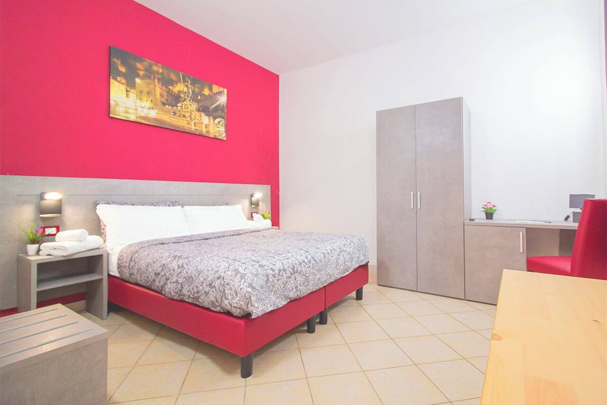 Ein modernes Schlafzimmer mit roter Akzentwand, einem großen Bett, einem Kleiderschrank und einem Schreibtisch.