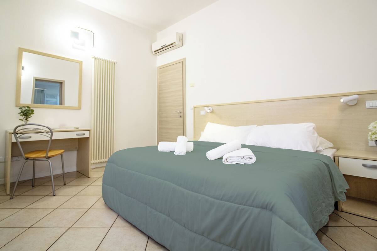 Ein Hotelzimmer mit Bett, Schreibtisch, Stuhl, Spiegel und Nachttisch.