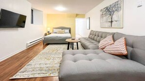 A modern living room with a grey sofa, a grey armchair, a small round table, and a bed with a grey headboard. - Le Plateau Boutique Apart Hotel (Montreal)