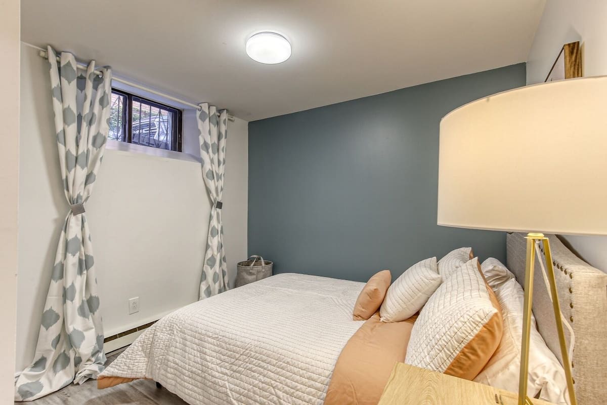 Un dormitorio con cama, cortinas, lámpara y ventana.