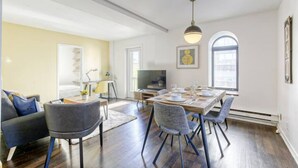 A dining area with a wooden table set for four, surrounded by chairs. There is a sofa and a television in the adjacent room. - Le Plateau Boutique Apart Hotel (Montreal)