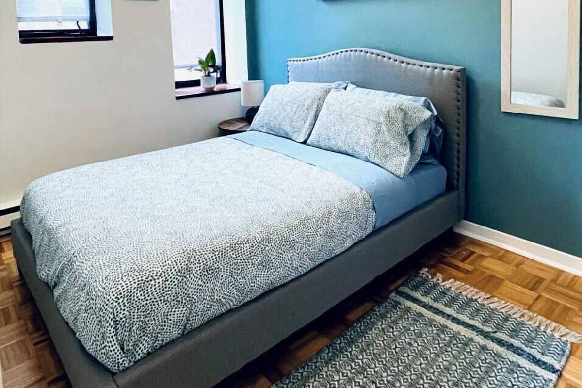 Un dormitorio con cama, ventana, cuadro y alfombra.