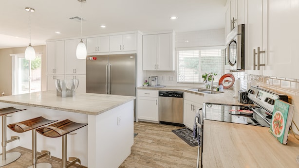 Una cocina moderna con armarios blancos, electrodomésticos de acero inoxidable y una isla central con taburetes de bar.