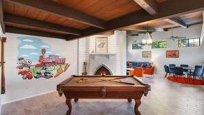 Une table de billard dans une pièce dotée d’une cheminée, d’une fresque murale et d’un coin repas avec des chaises bleues.