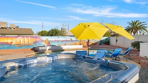 Un espace avec un jacuzzi agrémenté d’une fresque murale, une piscine et des chaises longues.