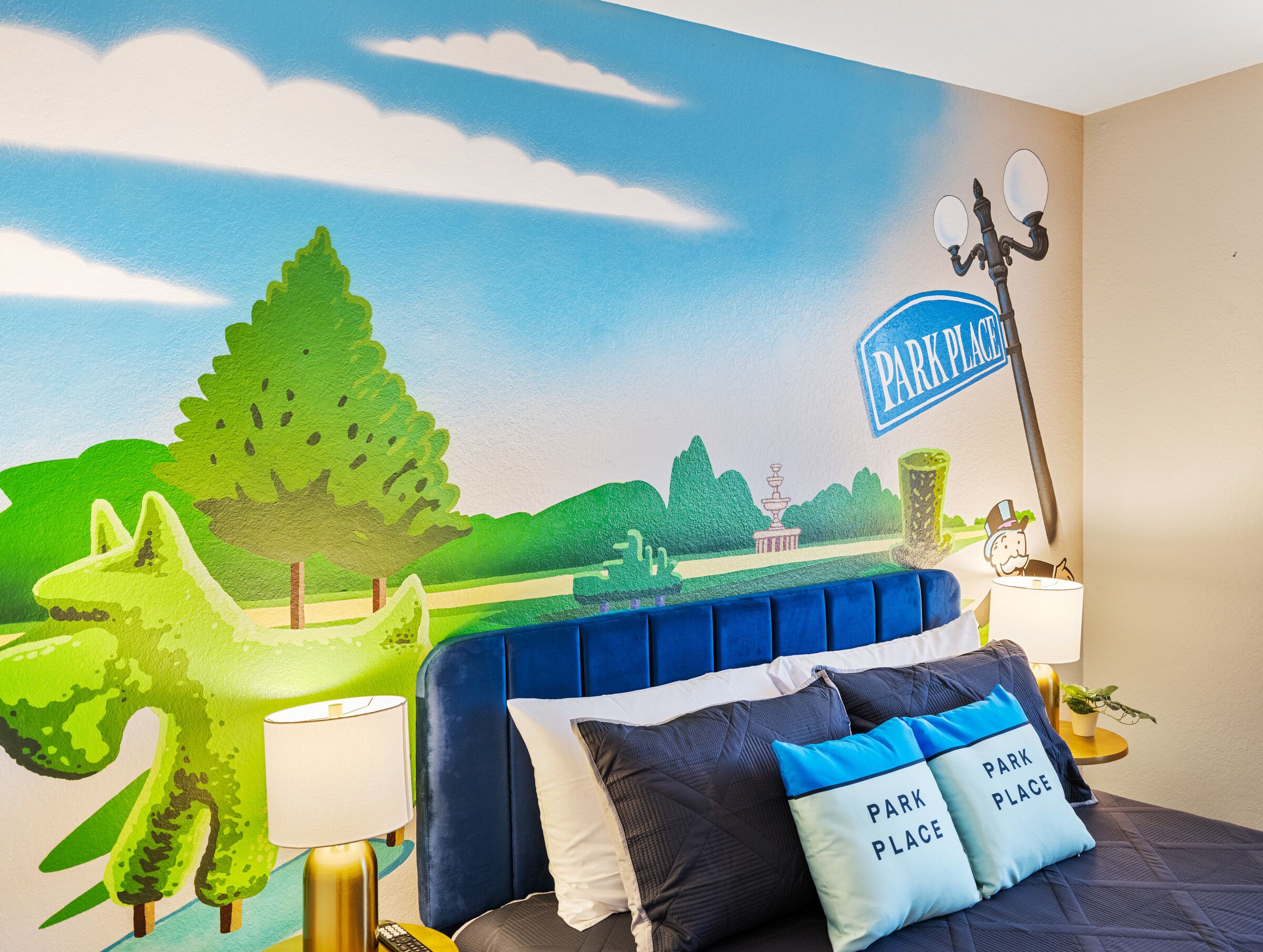 A bedroom with a mural of a park scene, a blue headboard, and a pillow with "PARK PLACE" text.
