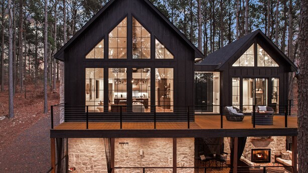Een houten chalet met twee verdiepingen, grote ramen, een stenen openhaard en buiten zitplaatsen.