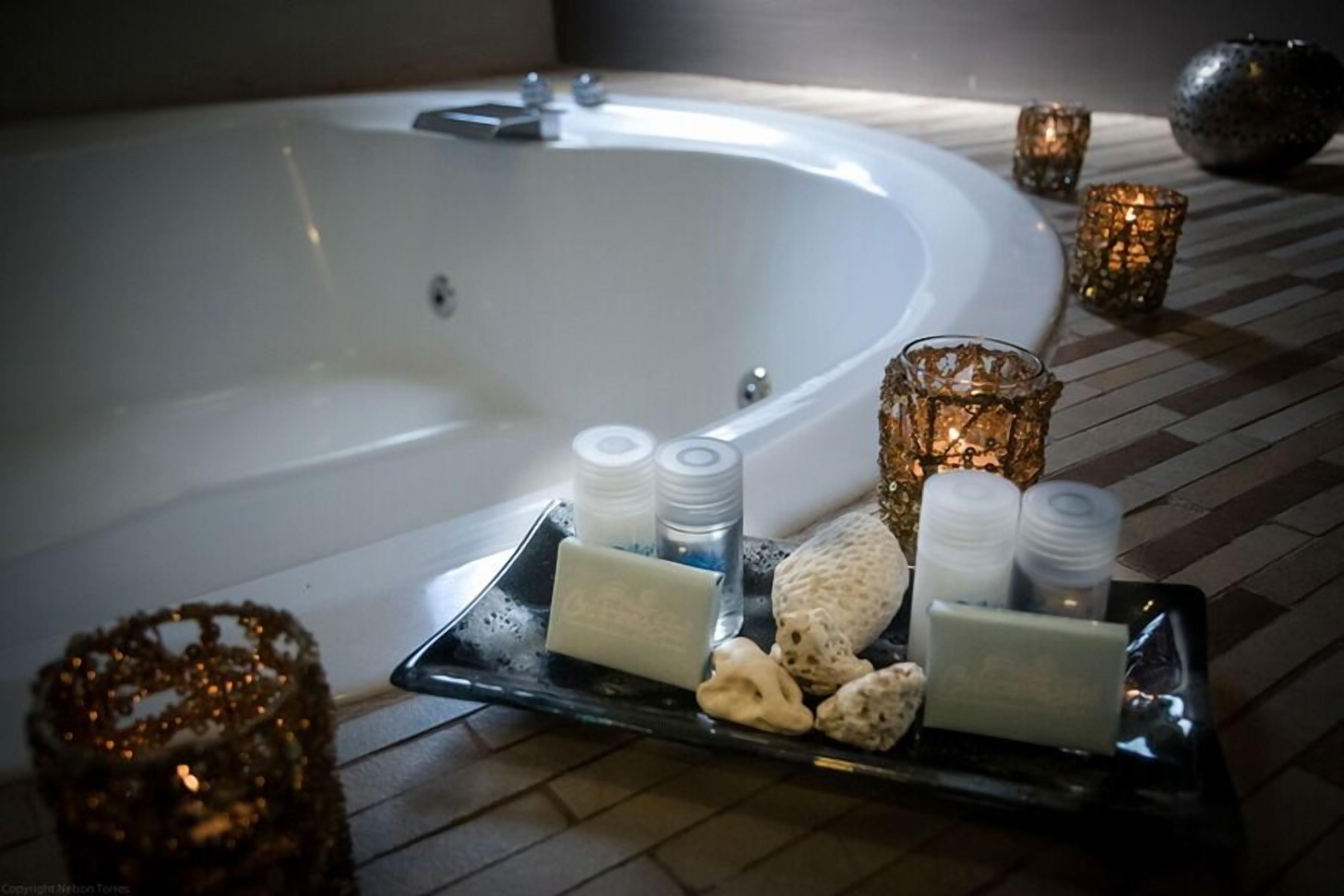 A spa area with a large bathtub, candles, and bath salts on a tray.