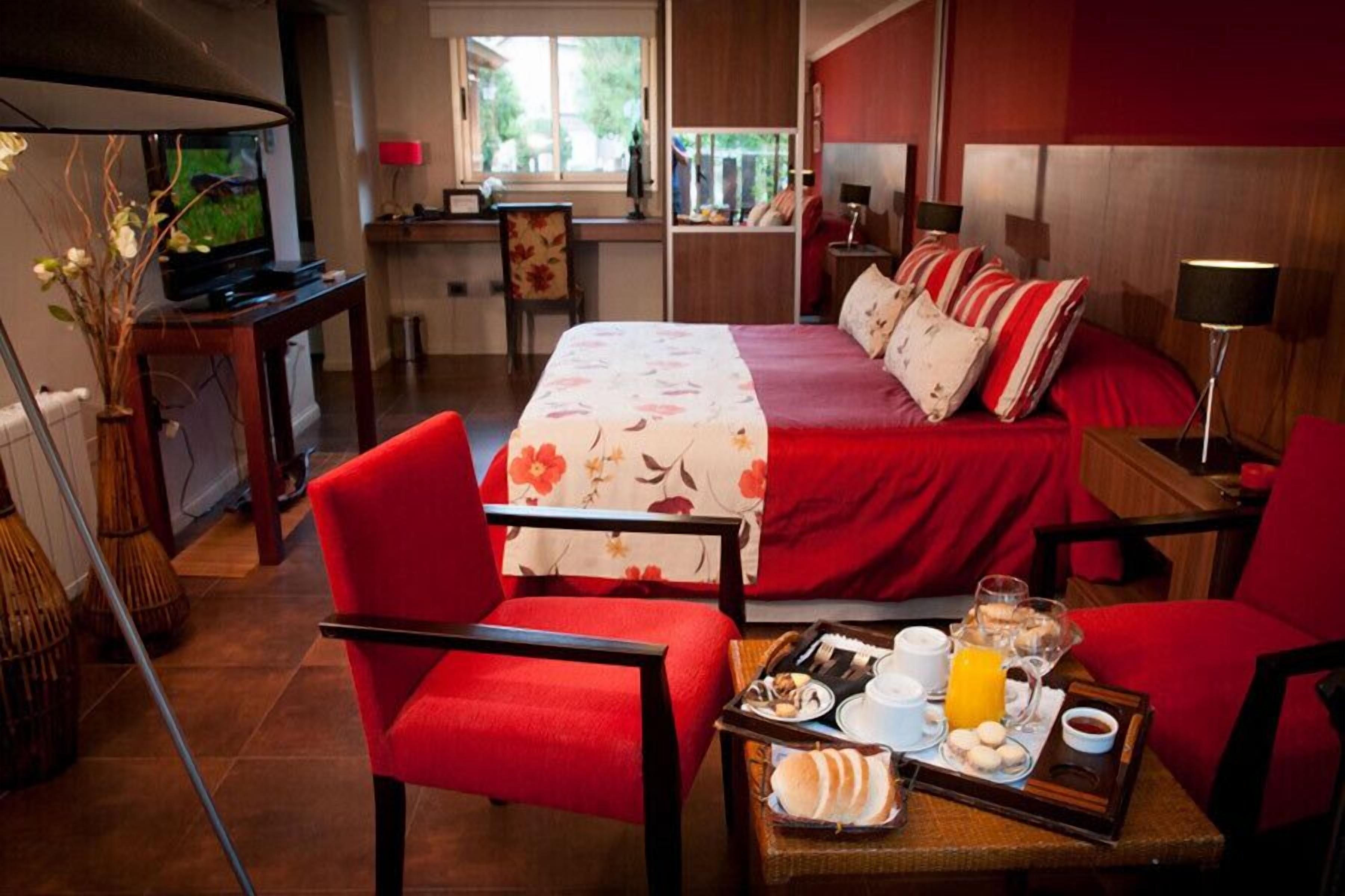 A hotel room with a bed, red chairs, a breakfast tray, and a TV.