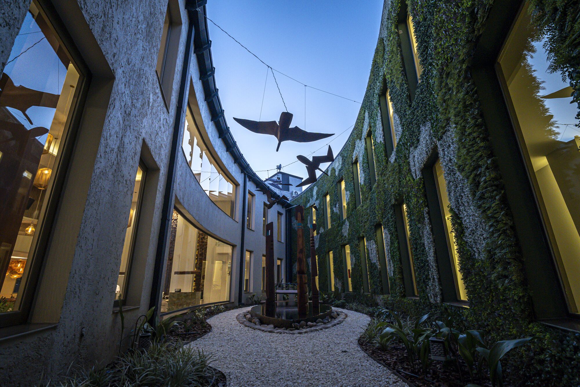 A courtyard with a central fountain, surrounded by buildings with large windows and greenery.