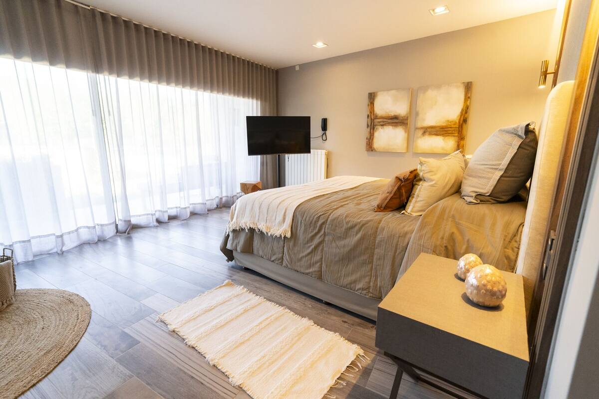 A modern bedroom with a large bed, a flat-screen TV, and artwork on the wall.